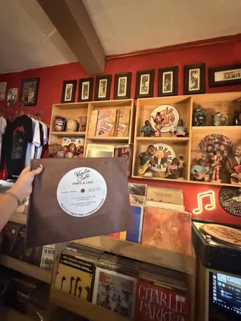 Disco con el logo de Vinilo & Café frente a una pared de LP